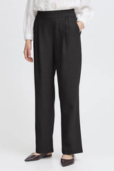 Person wearing black pants with a white shirt on a light gray background